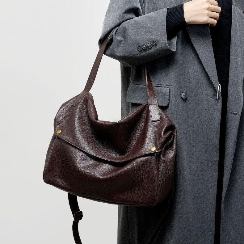 Coffee leather handbag held by a person wearing a gray coat on a light gray background