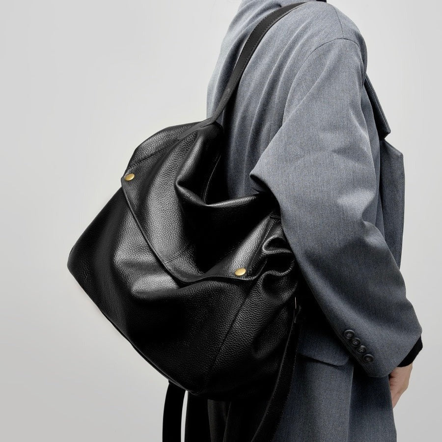 A person is carrying a black leather bag against a light gray background.