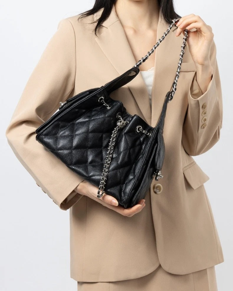 Person holding a black quilted handbag with a chain strap
