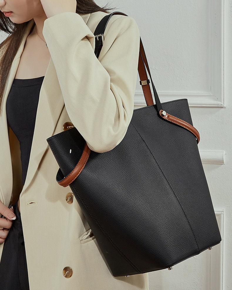Person holding a black handbag with brown handles and trim.