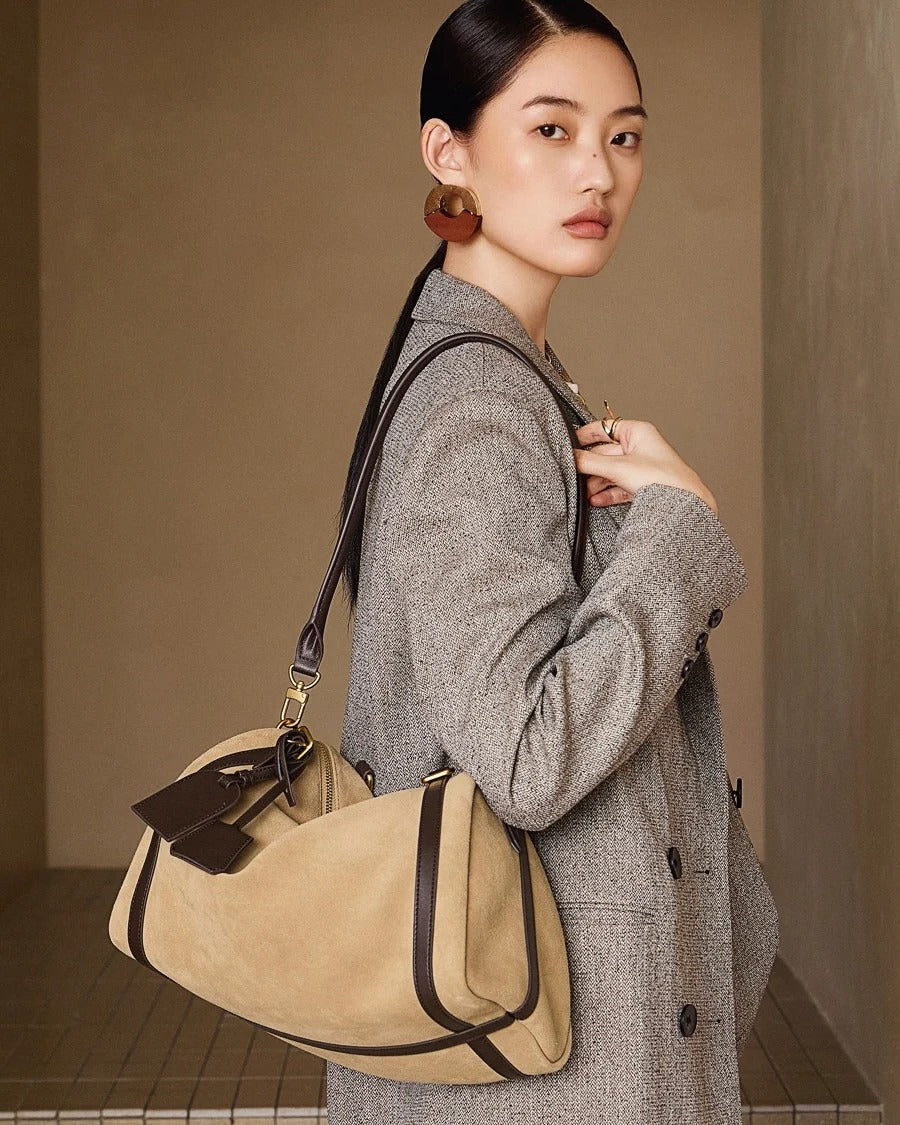 Woman holding a beige handbag with a brown strap against a neutral background