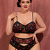 Women wearing a black lingerie set with red and pink floral pattern against a pink background