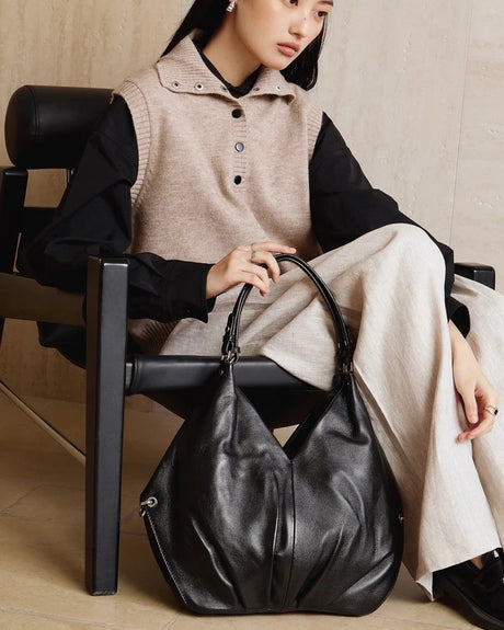 Woman sitting with a black leather handbag on a wooden floor.
