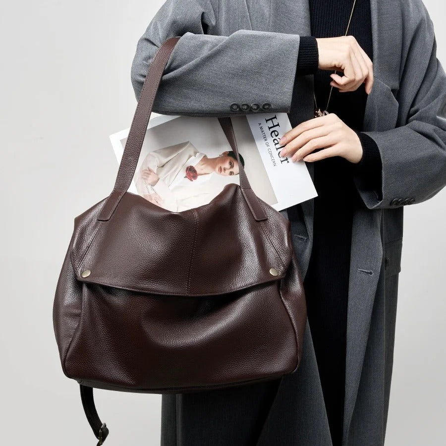 Person holding a Coffee leather bag with a magazine, wearing a gray coat on a light gray background