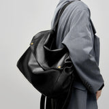 A person is carrying a black leather bag against a light gray background.