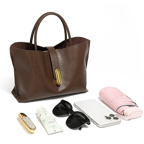 Coffee leather tote bag with phone, sunglasses, and other items on a white background