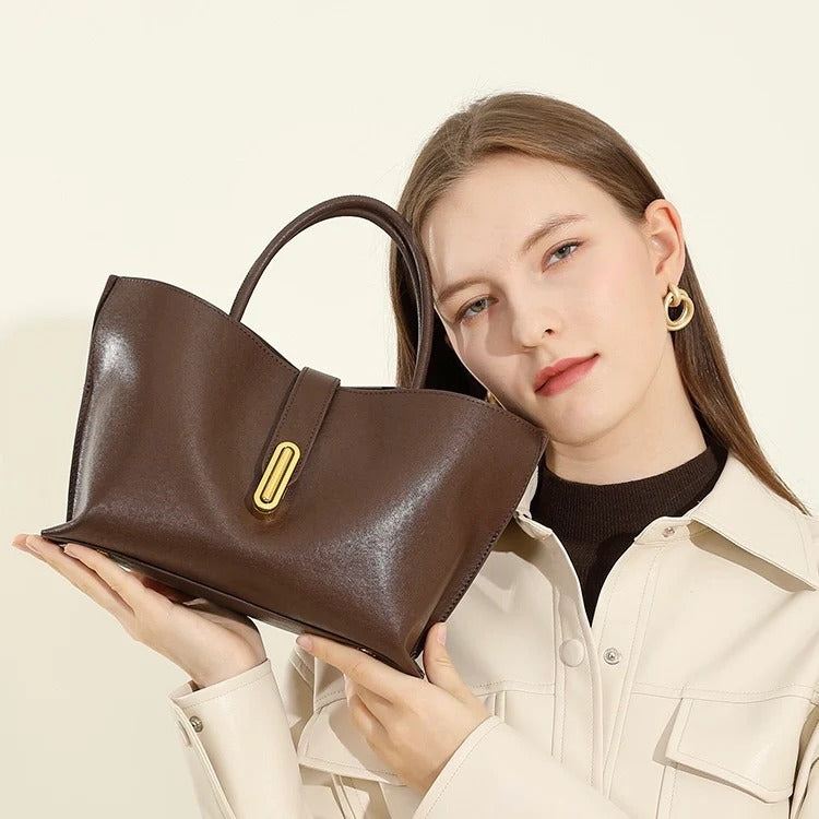 Woman holding a Coffee handbag with a gold clasp against a neutral background