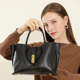 Woman holding a black handbag with gold accents against a neutral background