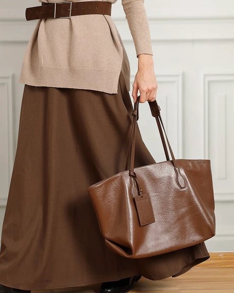 Person holding a brown leather handbag wearing a beige sweater and brown skirt.