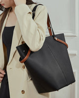 Person holding a black handbag with brown handles and trim.