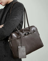 Person holding a chocolate leather handbag with a visible brand logo.