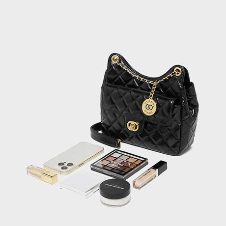 Black quilted handbag with gold chain and hardware, surrounded by makeup items 