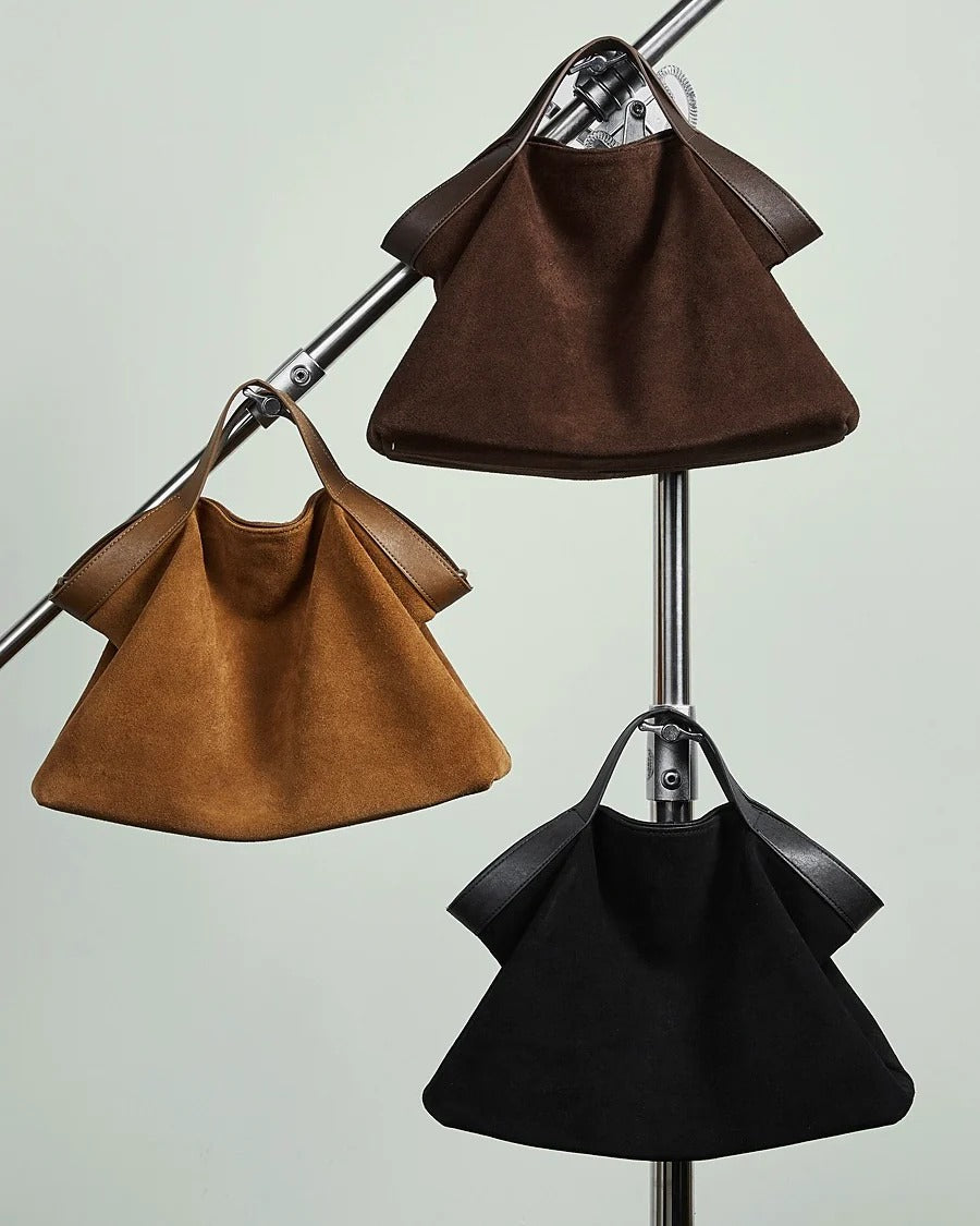 Three suede handbags in brown, black, and coffee hanging on a stand 
